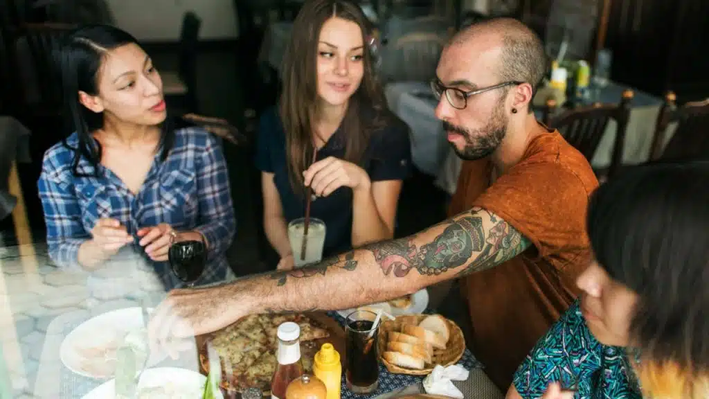 Four people sit around a table at a restaurant, sharing food and drinks.