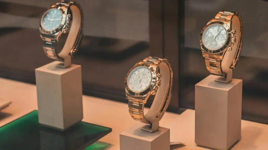A trio of rose-gold chronograph watches on pedestal stands.