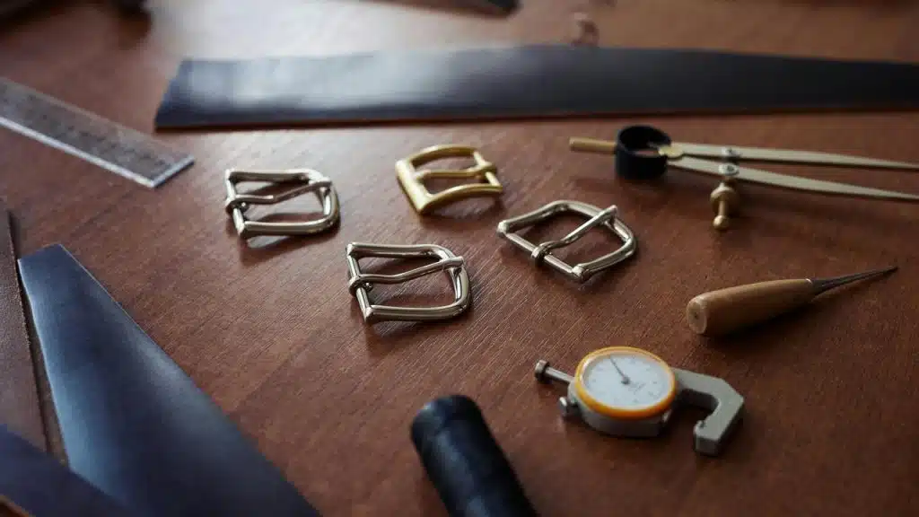 A collection of metal buckles and leatherworking tools on a wooden table.