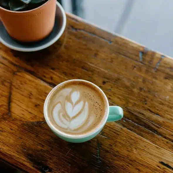 A cup of latte with heart-shaped latte art on a wooden table.