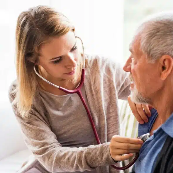 A young female doctor using a stethoscope to examine an elderly man.