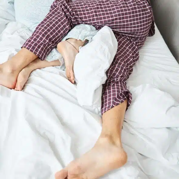 A child and an adult person's feet wearing pajamas while in bed.