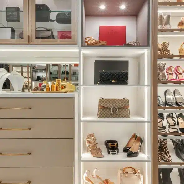 A well-lit, organized closet with shelves and drawers holding high-end shoes, purses, and accessories.