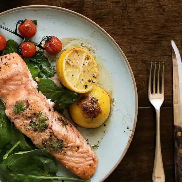 A plate of food with fish and vegetables placed beside a fork and a knife.