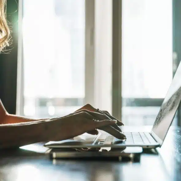 A person typing on a laptop near a window.