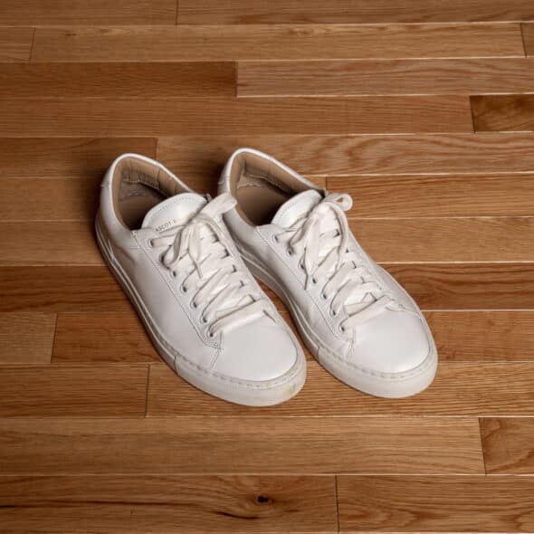 A pair of white sneakers with laces on a wooden floor.
