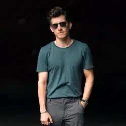 Man wearing a green t-shirt with grey pants standing with one hand in his pocket.