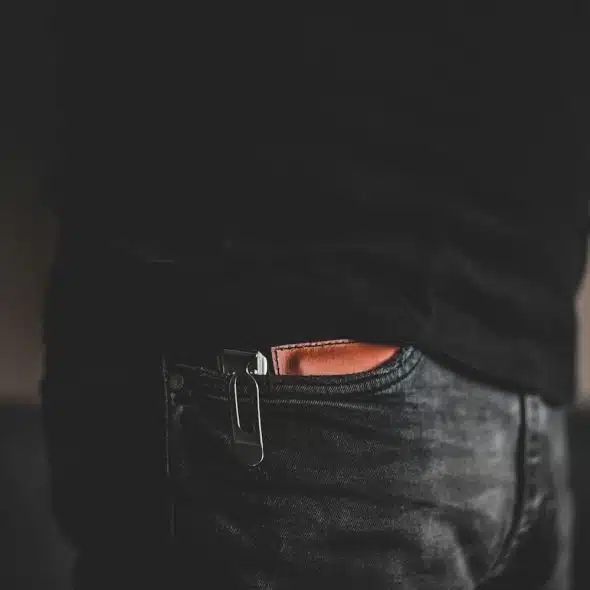 A brown wallet is seen tucked into the front pocket of a person's dark jeans.