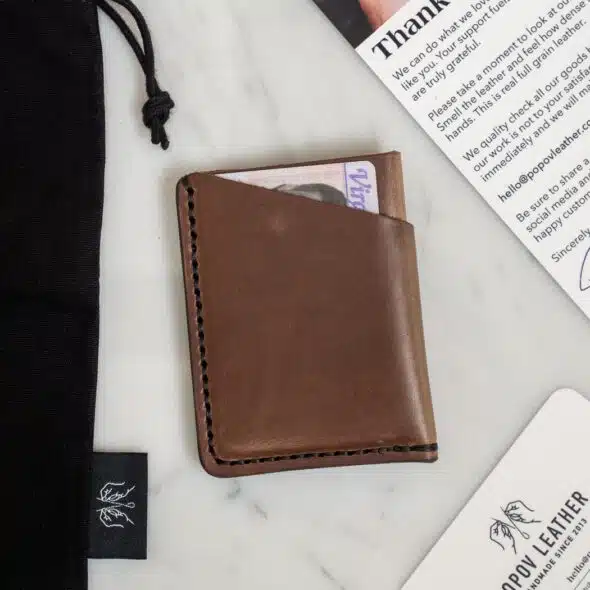 A brown leather wallet with cards inside, next to a black drawstring bag and a white card with text that begins with "Thank you."