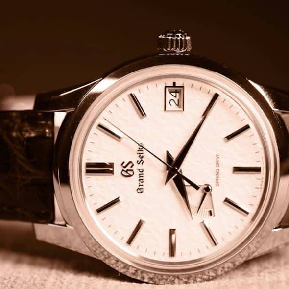 A close-up of a Grand Seiko watch with a white dial, a date window, and a brown leather strap.