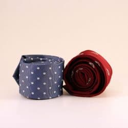 Two rolled neckties, one solid red and the other grey with dots, placed next to each other.