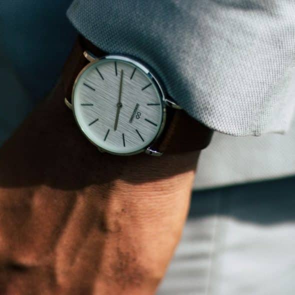 A minimalist watch with a white face and brown strap on a person's wrist.