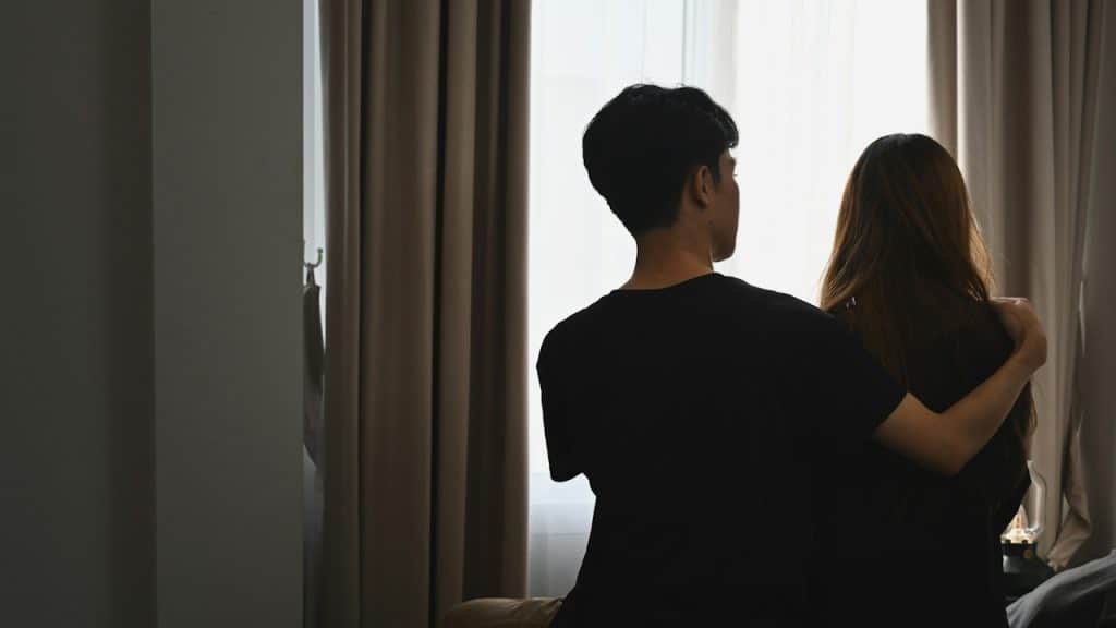 A young man embracing his girlfriend and sitting in the bedroom.