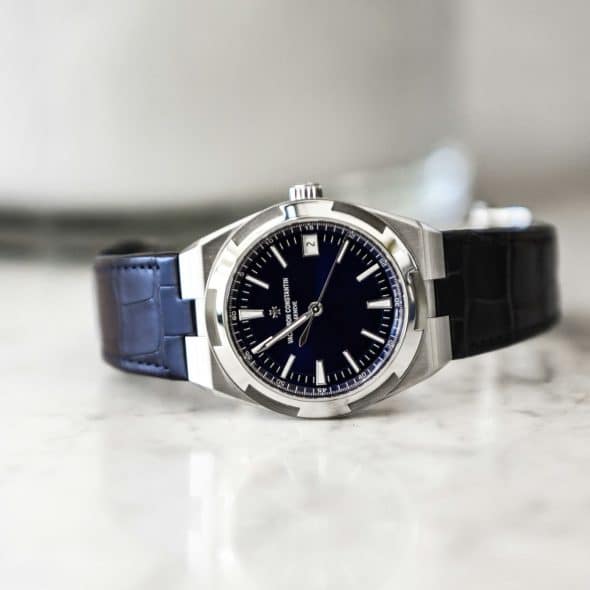 A Vacheron Constantin watch with a deep blue dial and black leather strap resting on a white marble surface.
