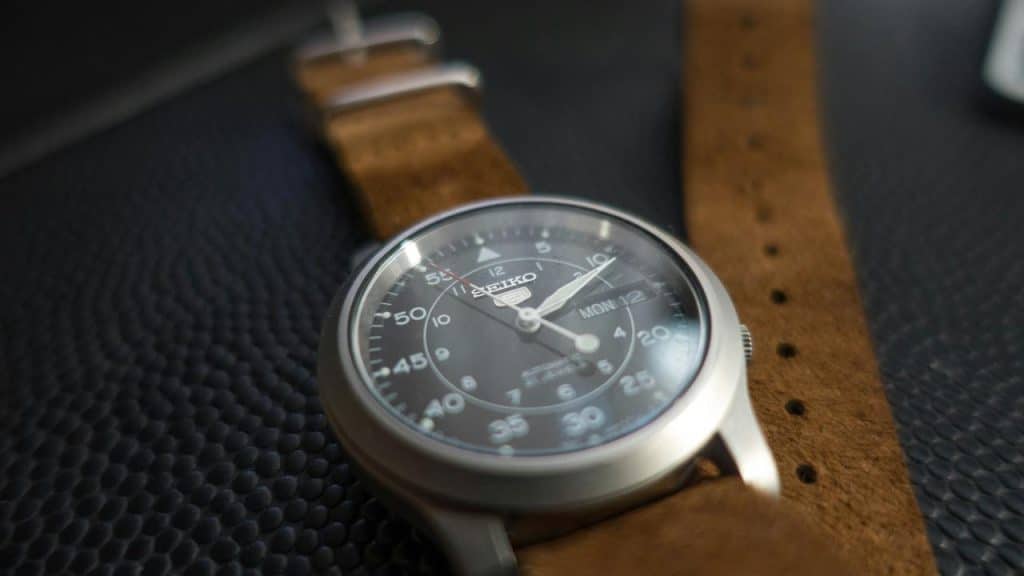 A silver-cased wristwatch with a brown leather strap resting on a black textured surface.