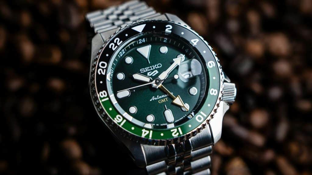 A GMT watch with a green dial and two-tone bezel on coffee beans.