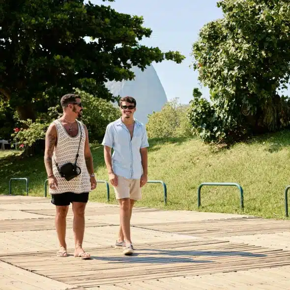 Two men walking and chatting on a wooden boardwalk beside a grassy park.