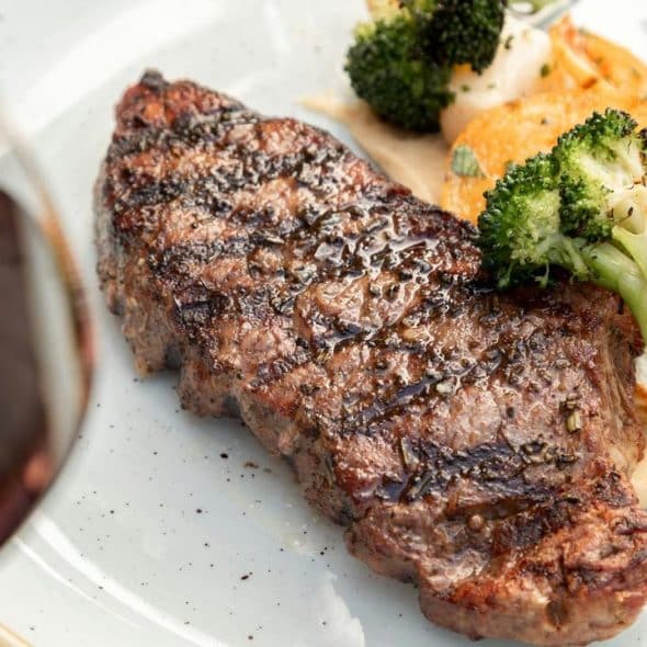 A grilled steak with broccoli, potatoes, and a glass of red wine.