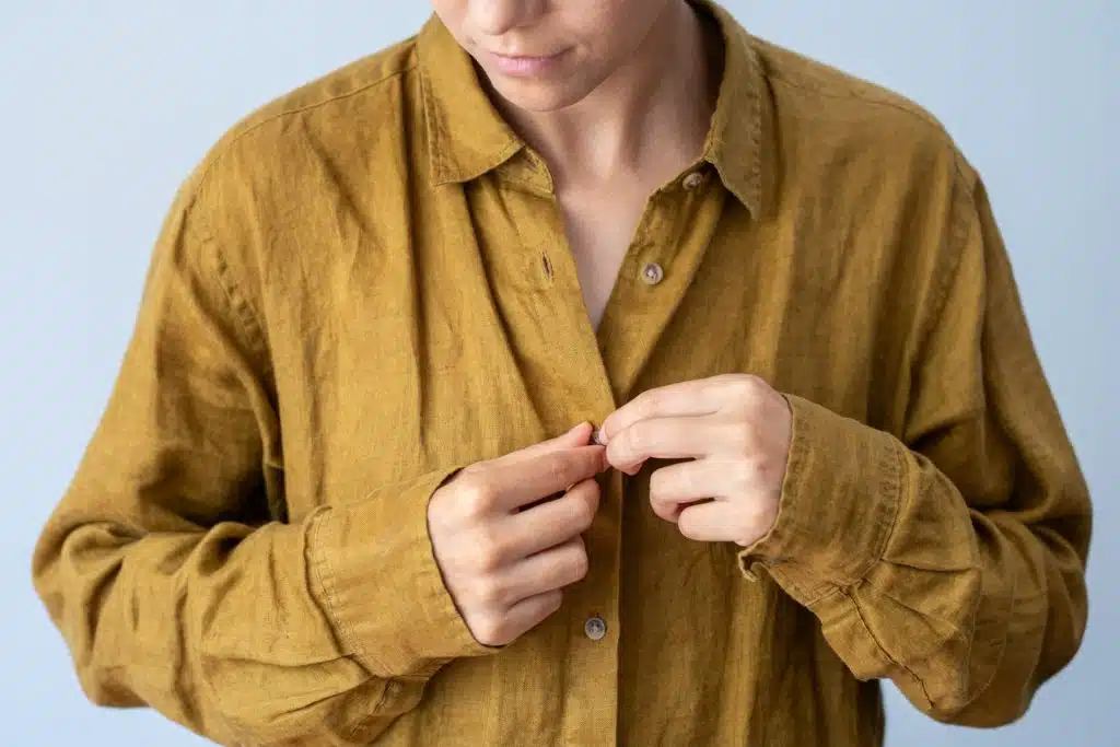 The man is closing the buttons of his brown shirt.