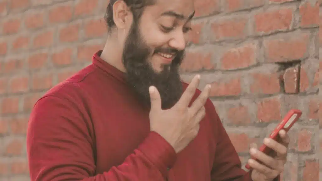 A man with a beard pointing using a cell phone.