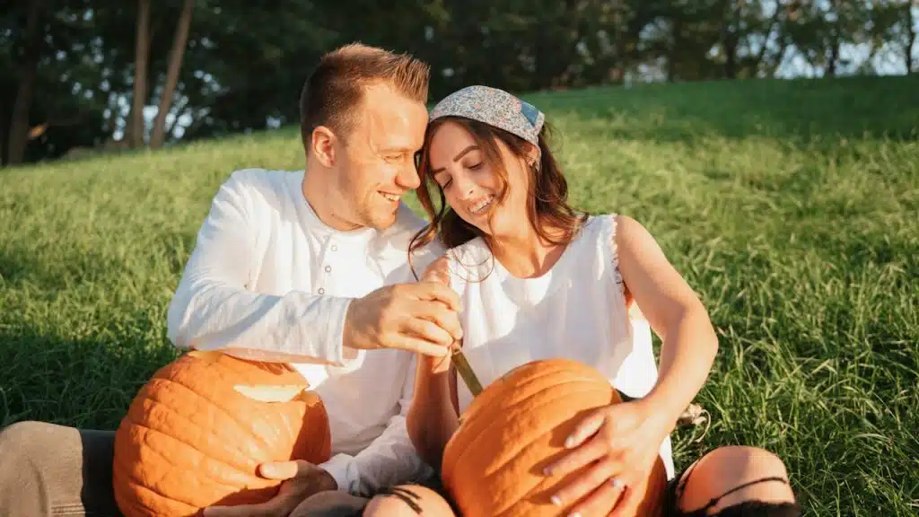 A couple caving pumpkins together on a grassy field.