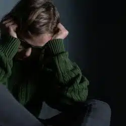 A person sitting with head down and hands covering their ears.