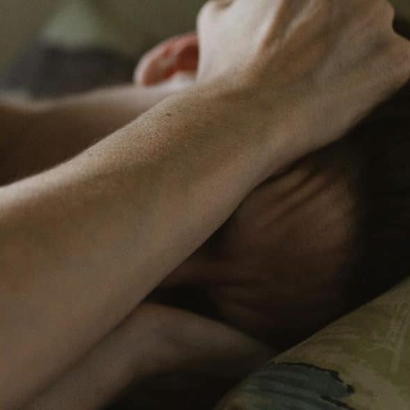 A person lying in bed with an arm covering their face.