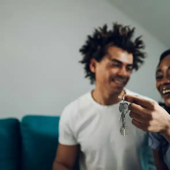 A smiling couple holding up a set of keys in a living room.