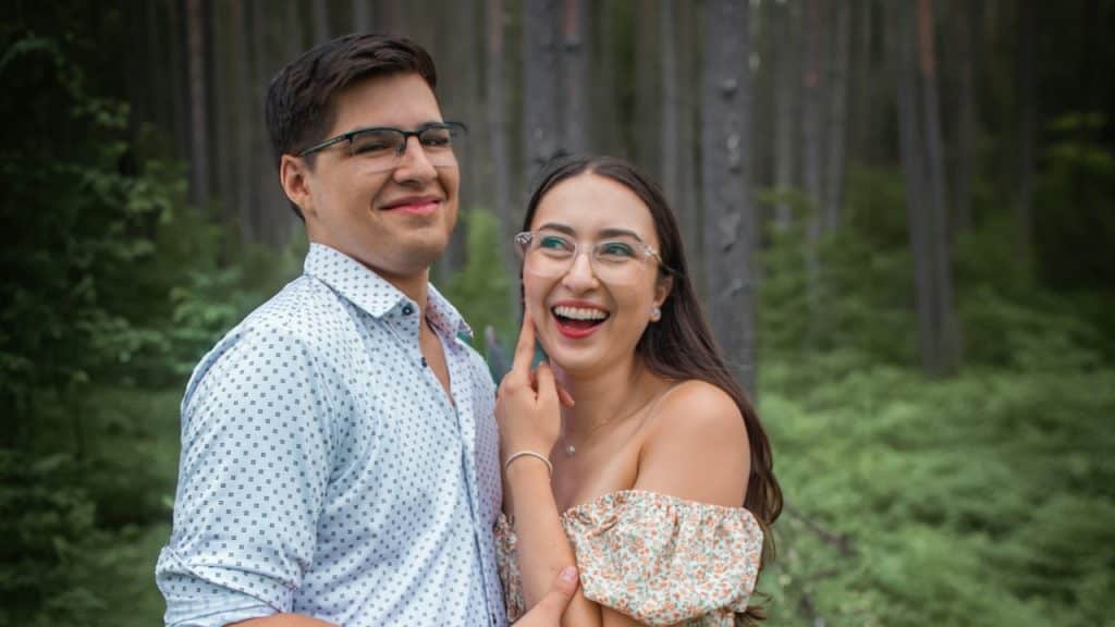 A man and a woman standing next to each other in a forest.