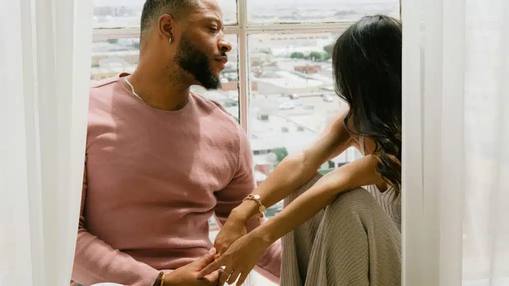 A man and a woman sitting on a window sill.