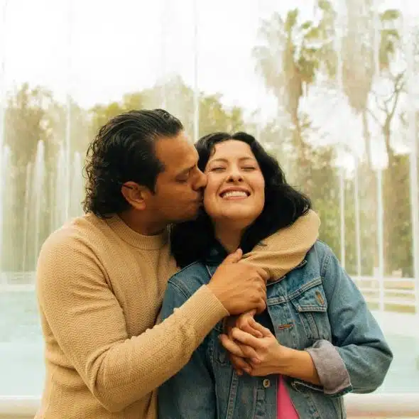 A couple hugging by a park fountain, smiling.