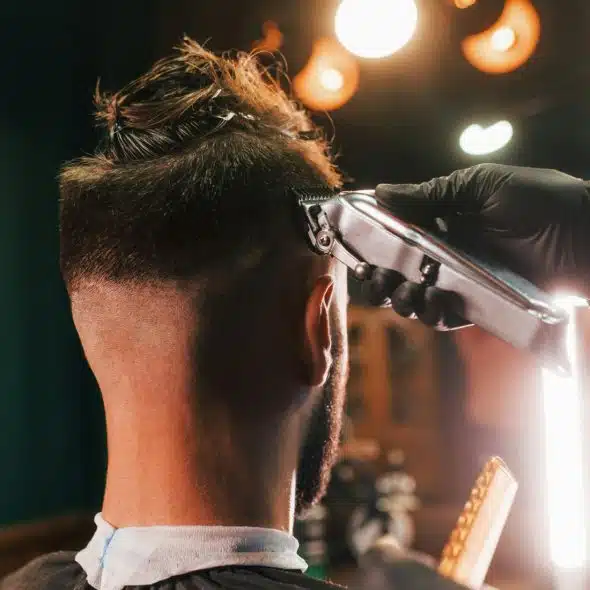 A man getting a haircut with a trimmer by a barber wearing black gloves.