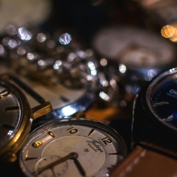 A collection of watches with various designs and colors scattered on a dark, reflective surface, creating bokeh effects from blurred lights.