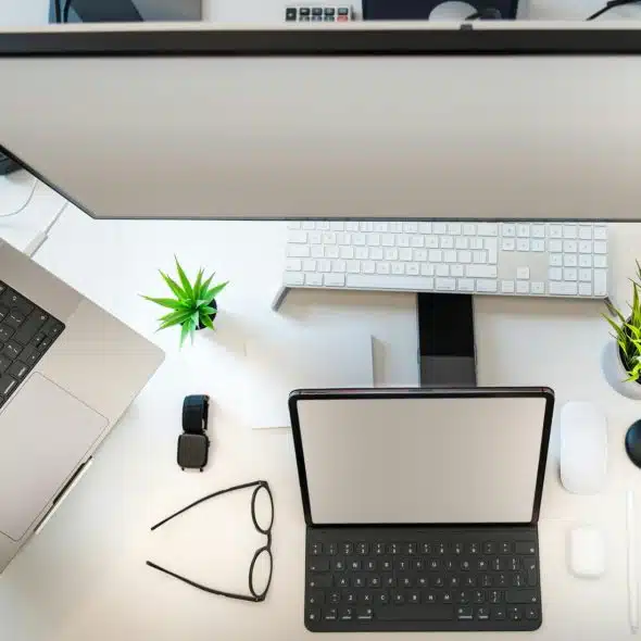 A birds-eye view of a desk setup with a laptop, monitor, keyboard, and other tech gadgets.