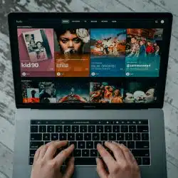 A person's hands typing on a silver laptop displaying the Hulu streaming service interface with various show thumbnails.