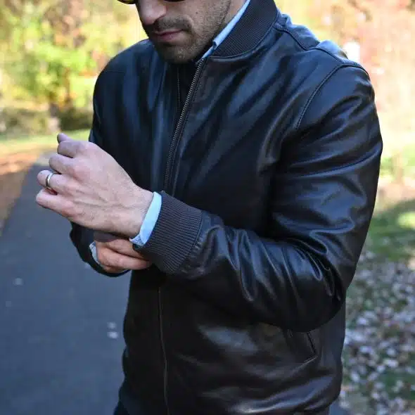 A close-up of a man wearing a black leather jacket and a light blue shirt.