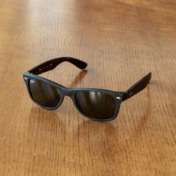A pair of black Ray-Ban New Wayfarer sunglasses with dark lenses resting on a wooden table.