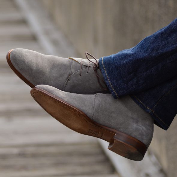 A close-up shot of a person's feet wearing gray suede chukka boots.