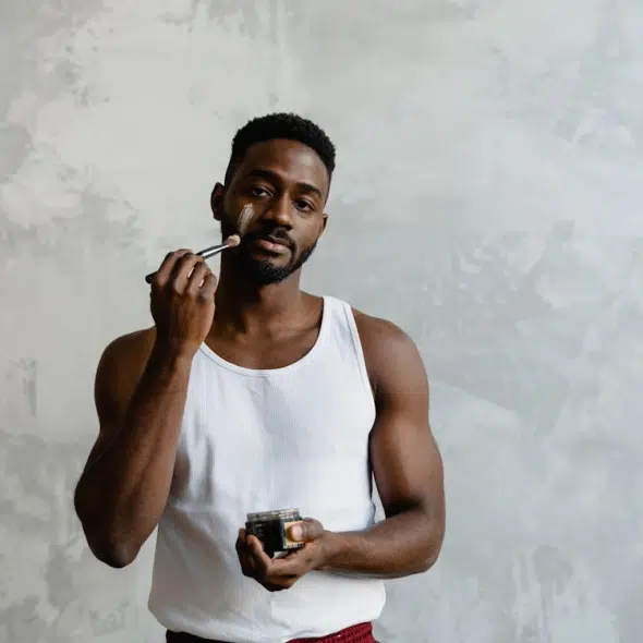 A Man in White Tank Top Applying a Face Mask on His Face Using a Brush