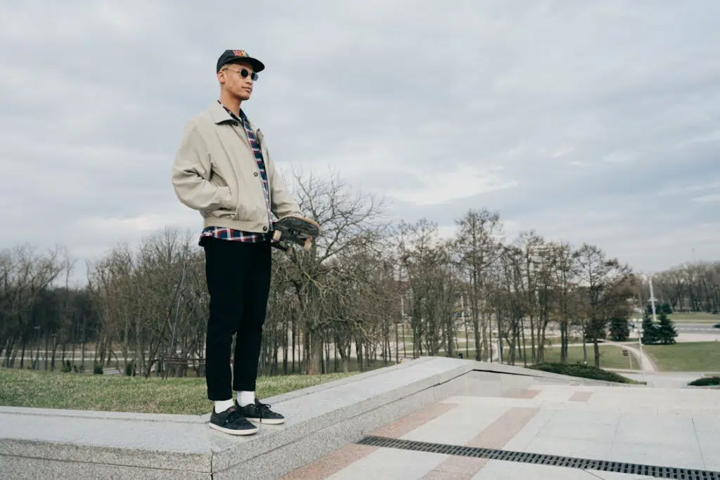 Young Man with a Skateboard Standing on a Wall on the Side of Steps in a Park